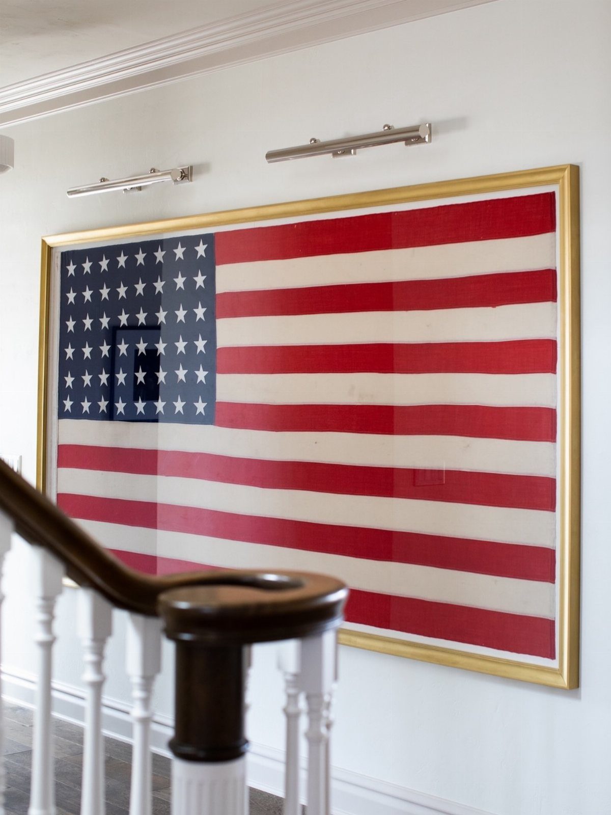American flag in a gold wooden frame hanging on a white wall.