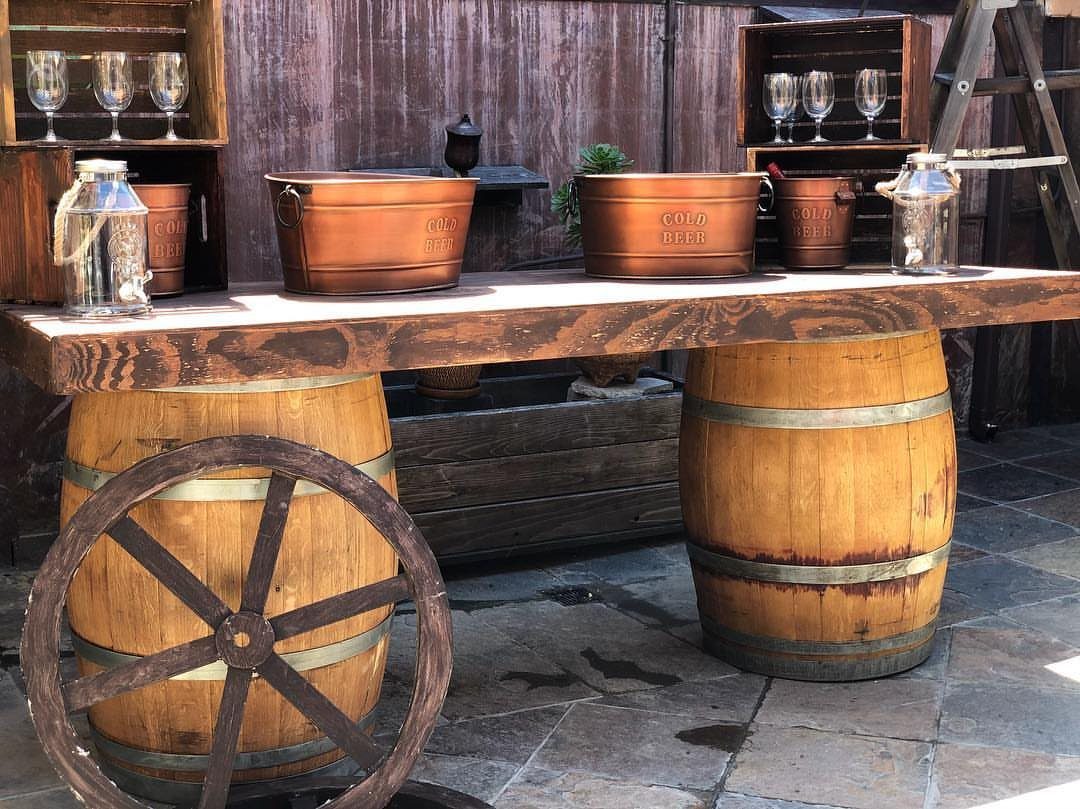 Rustic wooden beverage station with barrels, copper buckets, and a wagon wheel.