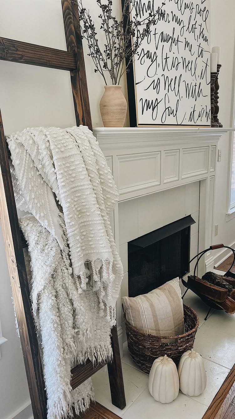 Wooden blanket ladder with a white knit throw leaning against a white fireplace.