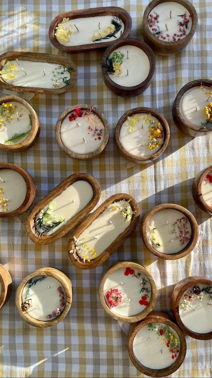 Handmade candles in wooden bowls with dried flowers on a checkered tablecloth