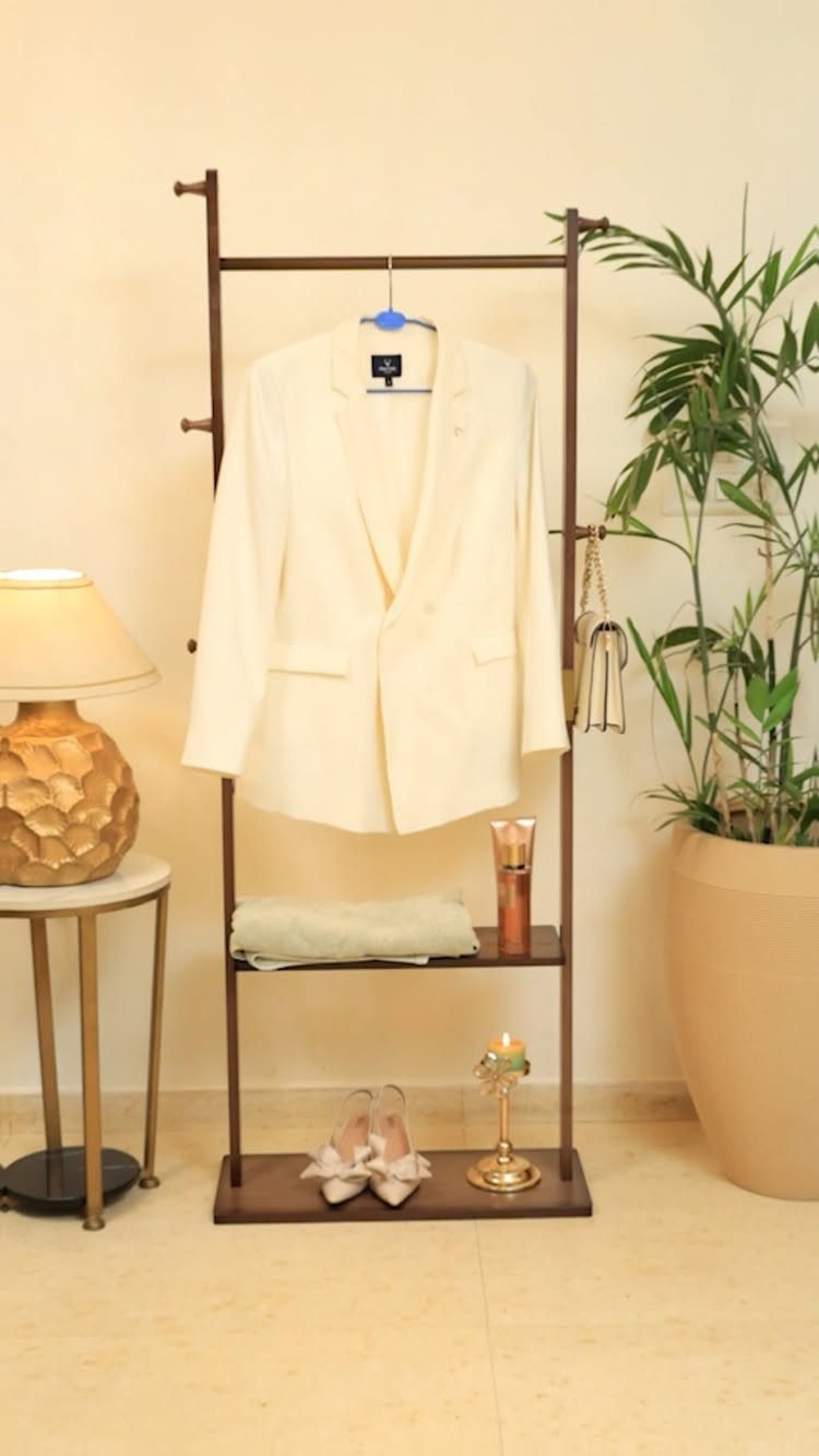 40 Home Decor Item Ideas, From Candle Holders to Sculptures 19 Wooden coat rack with a white blazer, shoes, and accessories in a room.
