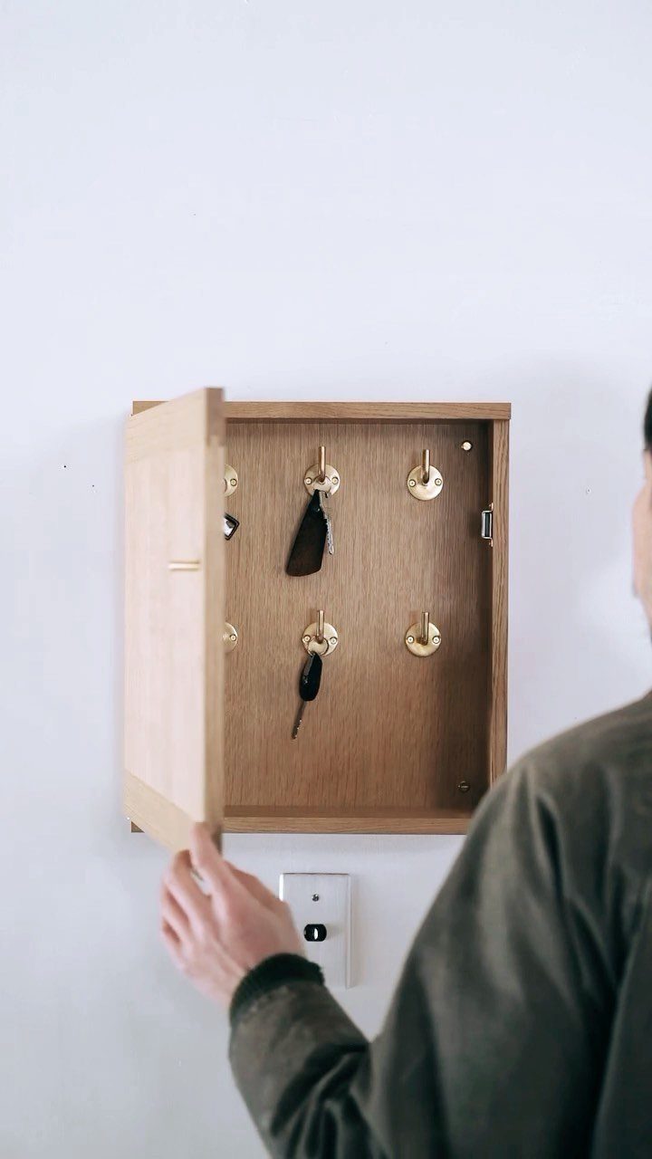 Wooden wall-mounted key organizer cabinet with keys hanging on hooks inside.
