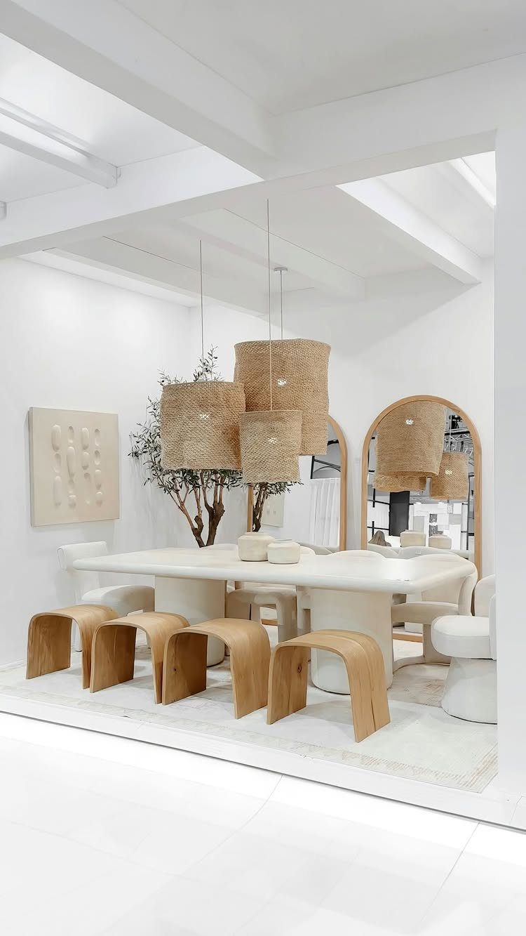 Woven pendant lights hanging over a white dining table with curved wooden stools.